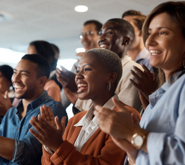 A united group of individuals clapping in an office, emphasizing their dedication to diversity and inclusion.