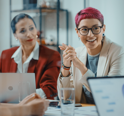 Two professional women sitting at a table, working on their laptops in business attire.