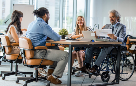 A diverse group engaged in leadership development, with a man in a wheelchair actively participating at a table.